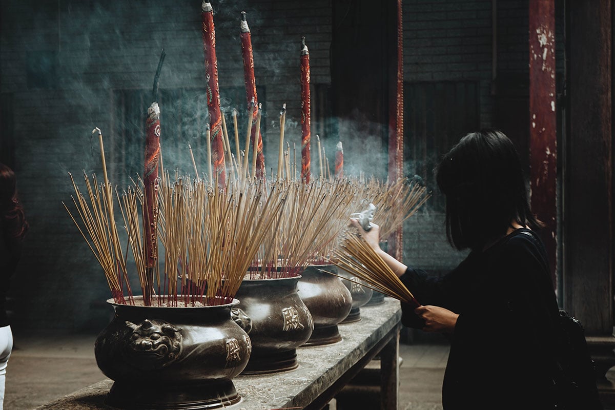 woman putting incense sticks on pot in vietnam